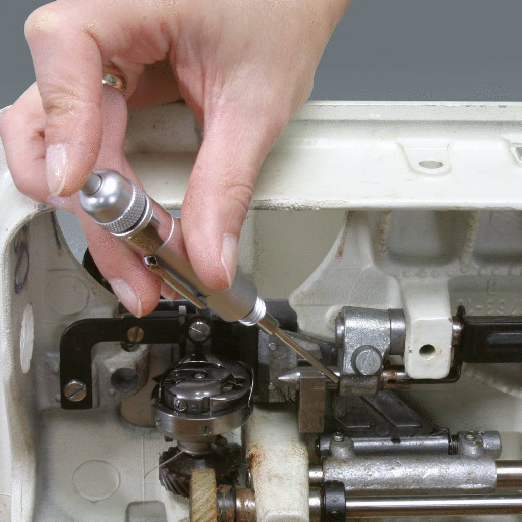 Ręka naprawia wnętrze maszyny do szycia śrubokrętem i małą szczoteczką, prezentując precyzję i pracę mechanika.