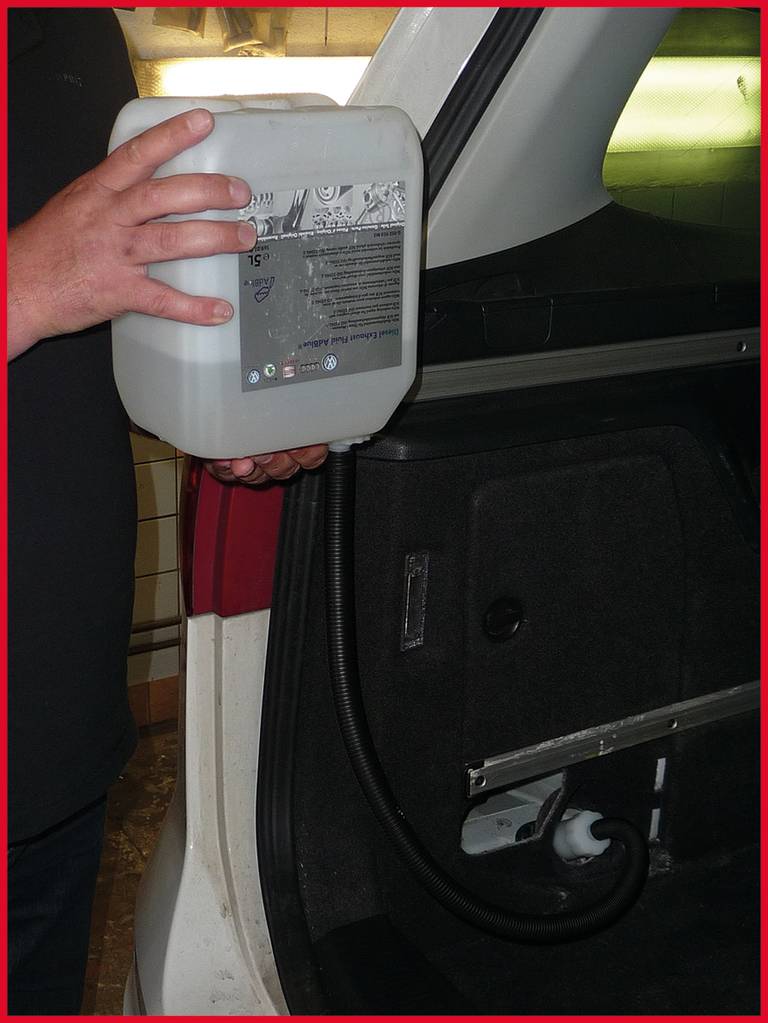 Osoba wlewa płyn AdBlue do zbiornika samochodu. Pojemnik z AdBlue jest trzymany w otwartym bagażniku.