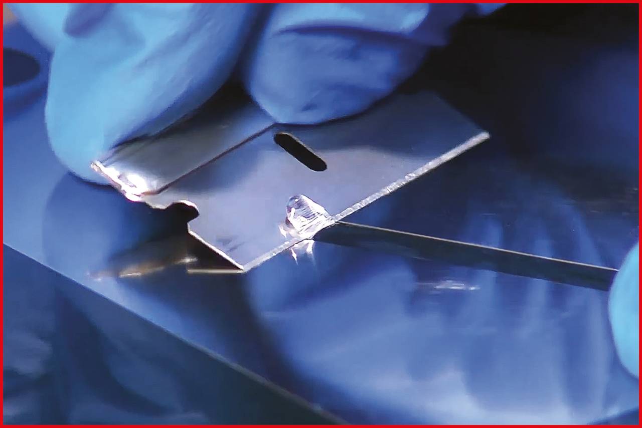 Zbliżenie dłoni w rękawiczce, która używa ostrza żyletki do przecięcia cienkiej folii lub warstwy na powierzchni.