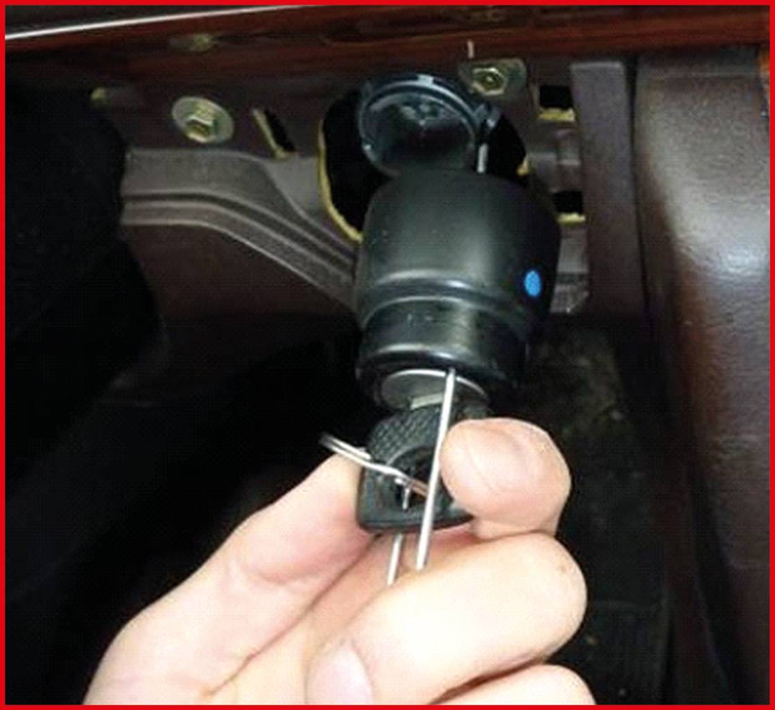 Dłoń trzyma kluczyk zapłonowy samochodu wraz z narzędziem. Stacyjka jest zdemontowana i ukazuje swój mechaniczny układ wewnętrzny.