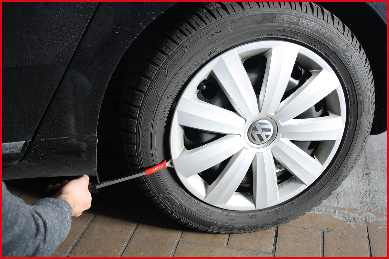 Człowiek używa przyrządu do pomiaru ciśnienia powietrza, aby sprawdzić ciśnienie w oponie samochodu. Opona ma srebrny felgę.