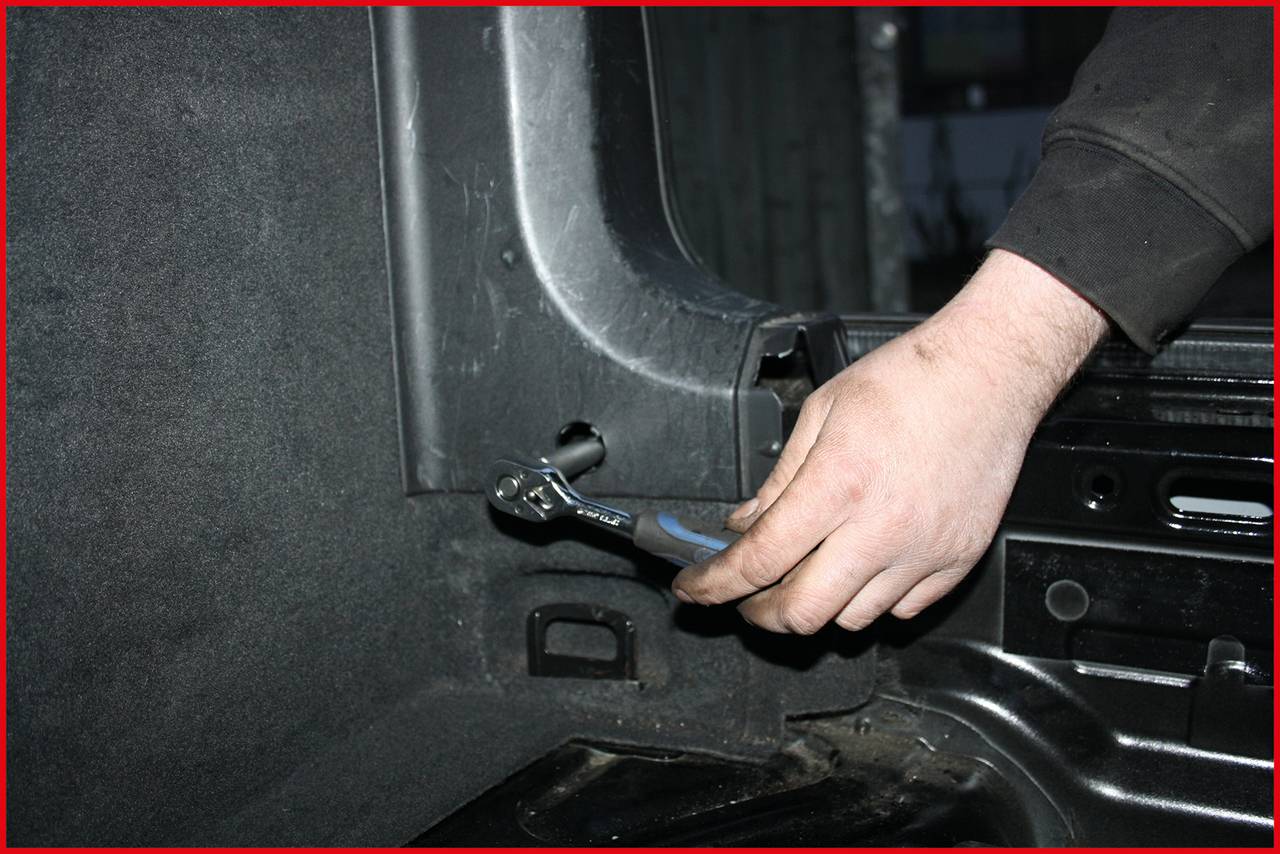 Osoba dokręca śrubę kluczem w bagażniku samochodu.