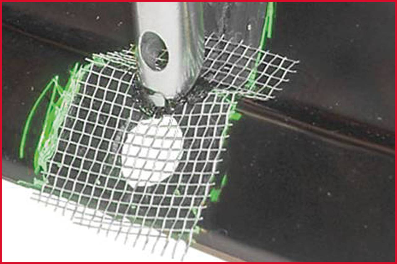 Metalowy hak jest przepychany przez kwadratową siatkę zamocowaną nad czarną powierzchnią.