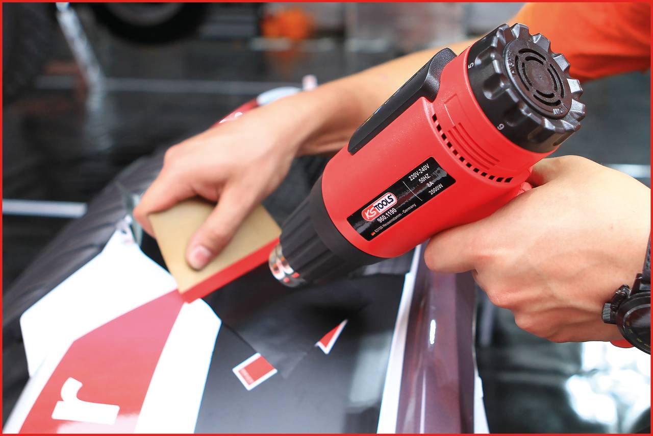 Osoba używa pistoletu na gorące powietrze, aby nanieść folię klejącą na powierzchnię.