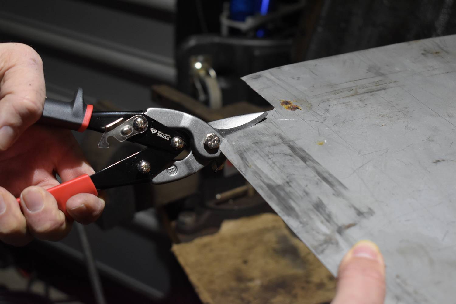 Osoba przycina kawałek blachy metalowej nożycami do metalu. Ręce trzymają nożyce, podczas gdy metal jest cięty.