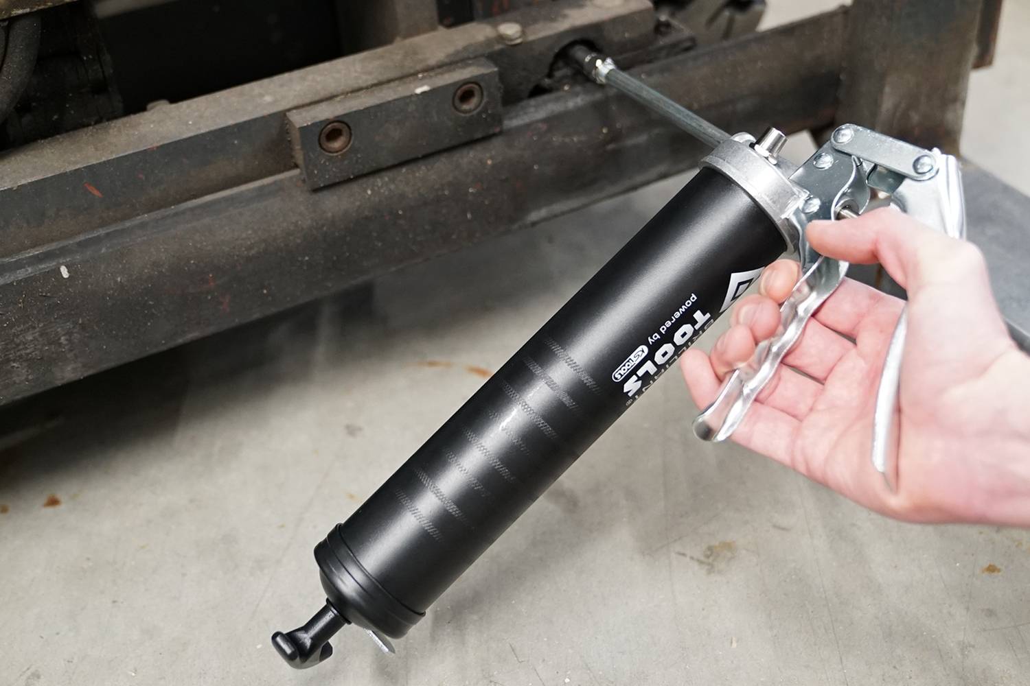 Jedna ręka trzyma czarną smarownicę i smaruje metalową oś.