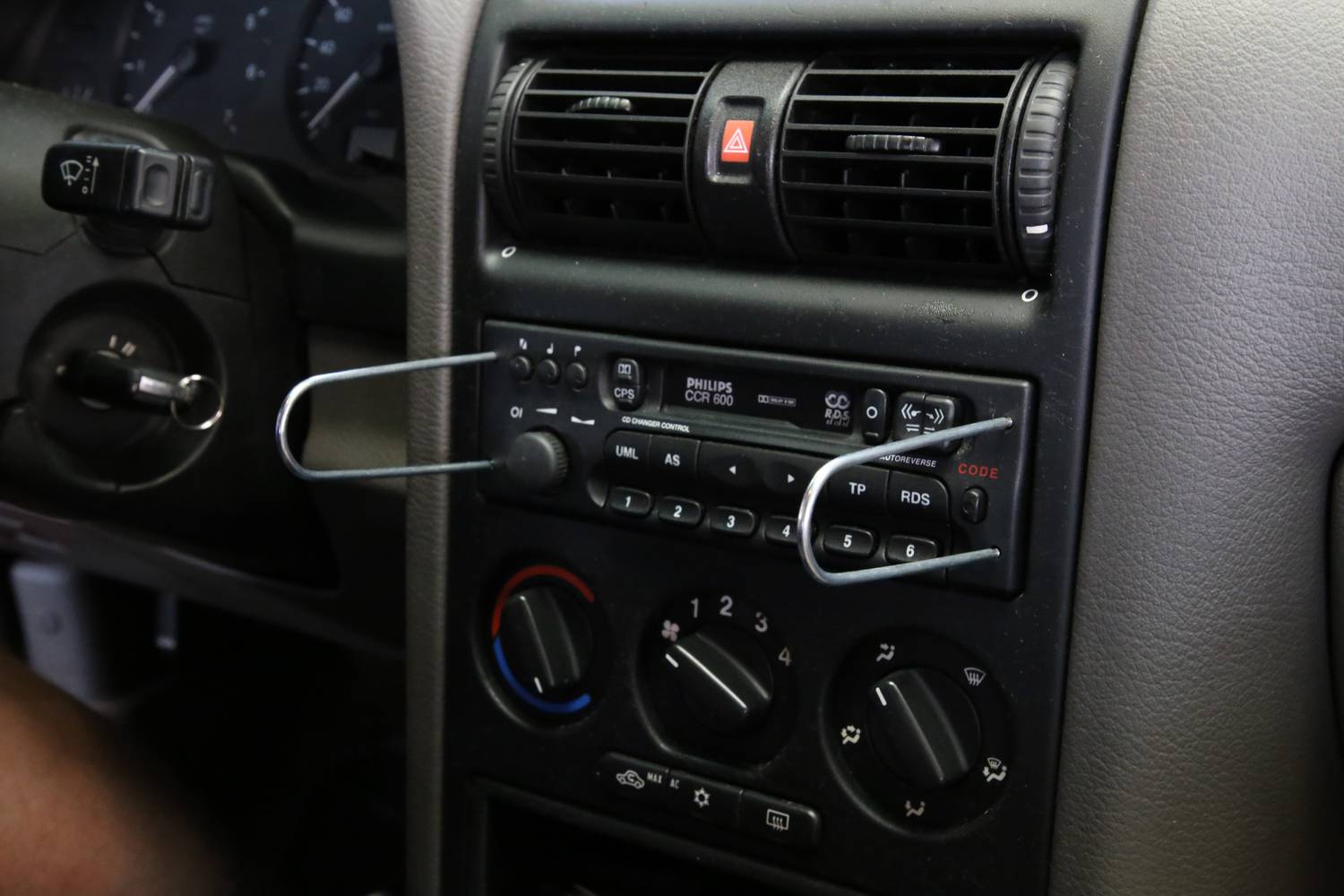 'Wyjmowanie radia samochodowego: spinacze włożone w otwory konsoli, aby wyjąć radio, deska rozdzielcza i elementy sterujące widoczne.'