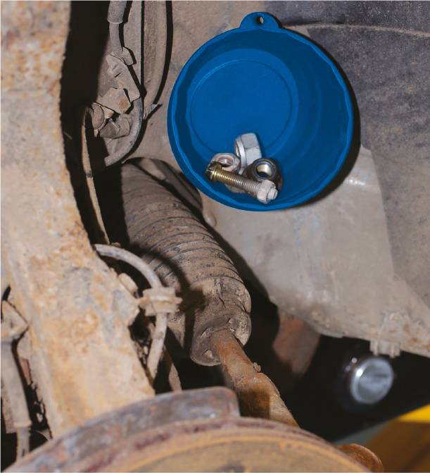 Niebieski plastikowy dekiel jest przymocowany do spodu pojazdu za pomocą śrub i nakrętki. Widoczne części są skorodowane.