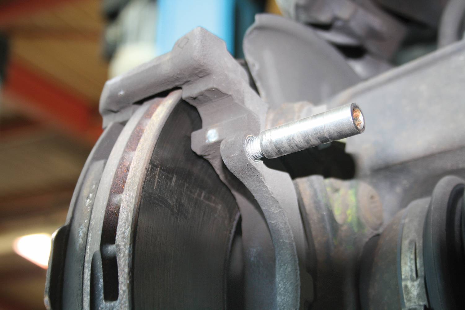 Zbliżenie tarczy hamulcowej z klockiem hamulcowym i śrubą mocującą, ukazujące zużycie na krawędzi tarczy w warunkach warsztatowych.