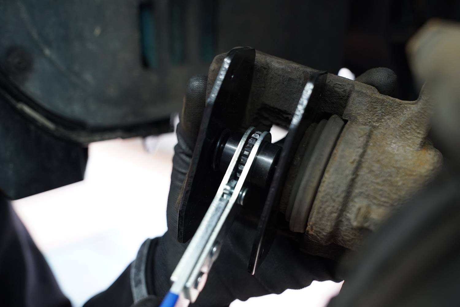 Osoba naprawia hamulce pojazdu za pomocą szczypiec, pracujących na zacisku hamulcowym i tarczy hamulcowej.