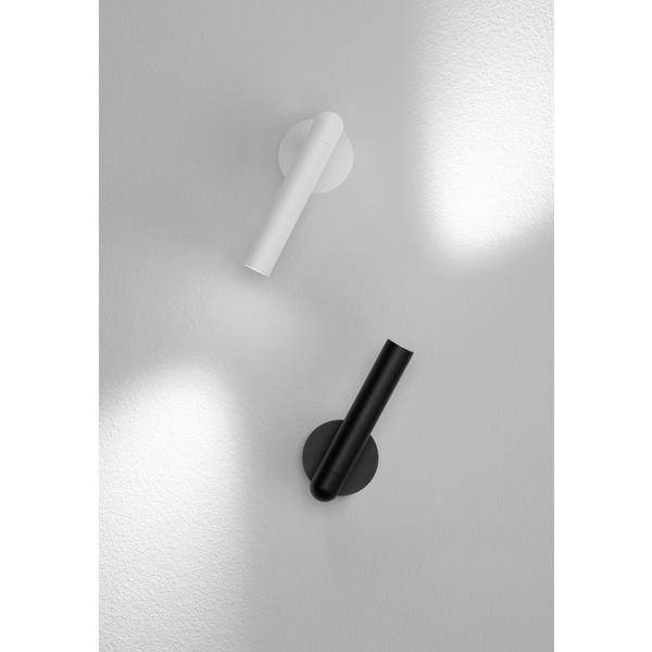 Dwie cylindryczne lampy ścienne, jedna biała, druga czarna, zamontowane na ścianie. Każda z nich rzuca snop światła w górę i w dół.