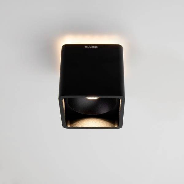 Czarna, kwadratowa lampa sufitowa z podświetlaną krawędzią, która świeci ciepłym, jasnym światłem, zamontowana na białym suficie.