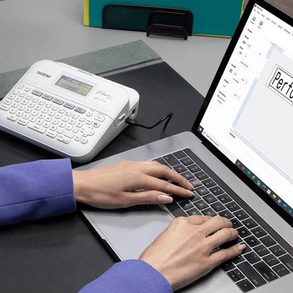 Osoba pisze na laptopie obok urządzenia do etykietowania.
