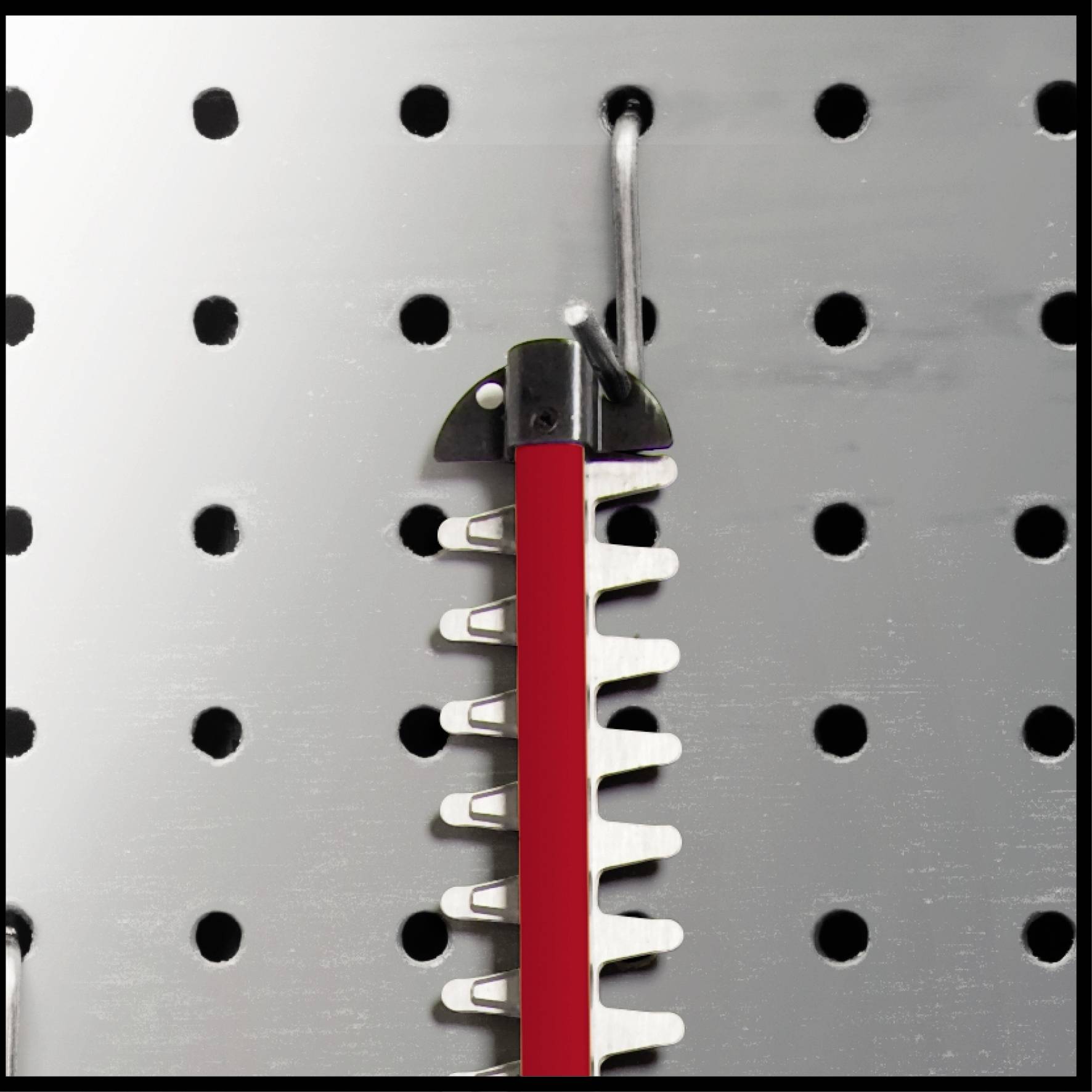 Czerwone narzędzie wisi na haku na tablicy perforowanej. Posiada ząbkowane metalowe krawędzie, które nadają się do prac tnących.