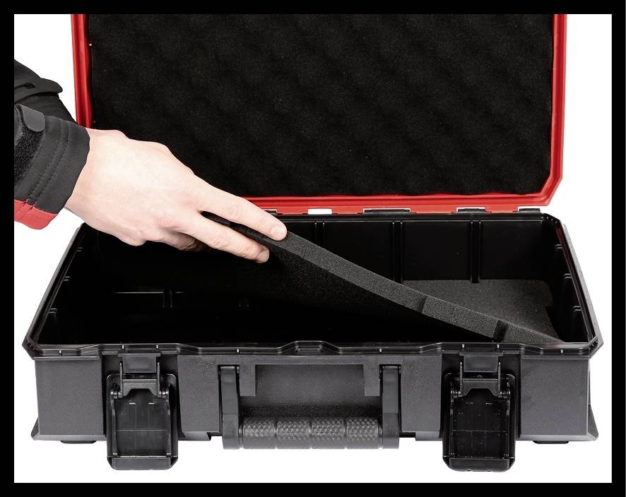 Dłoń wkłada wkładkę z pianki do pustego, otwartego czarnego walizki na narzędzia z czerwoną krawędzią.