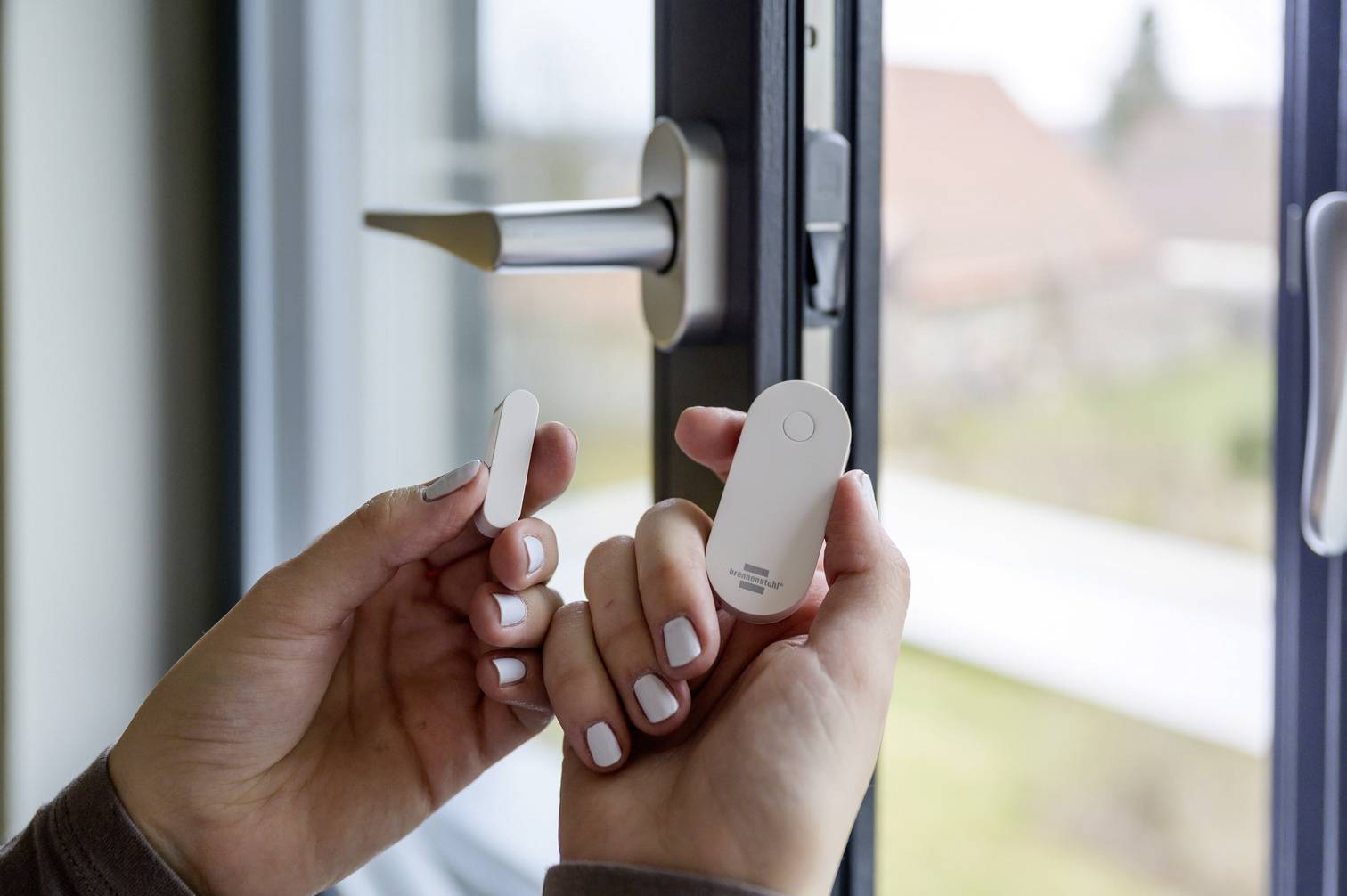 Osoba instaluje czujnik drzwiowy lub okienny przy otwartym oknie. Czujnik służy do monitorowania ruchu otwarcia.