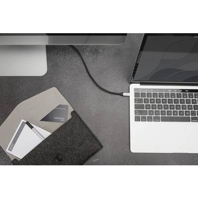 Laptop podłączony kablem do komputera stacjonarnego. Obok niego filcowa torba z notatnikami na szarym stole.