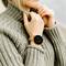 Osoba ubrana w szary sweter z dzianiny nosi smartwatch na nadgarstku, który wyświetla godzinę, tętno i liczbę kroków.