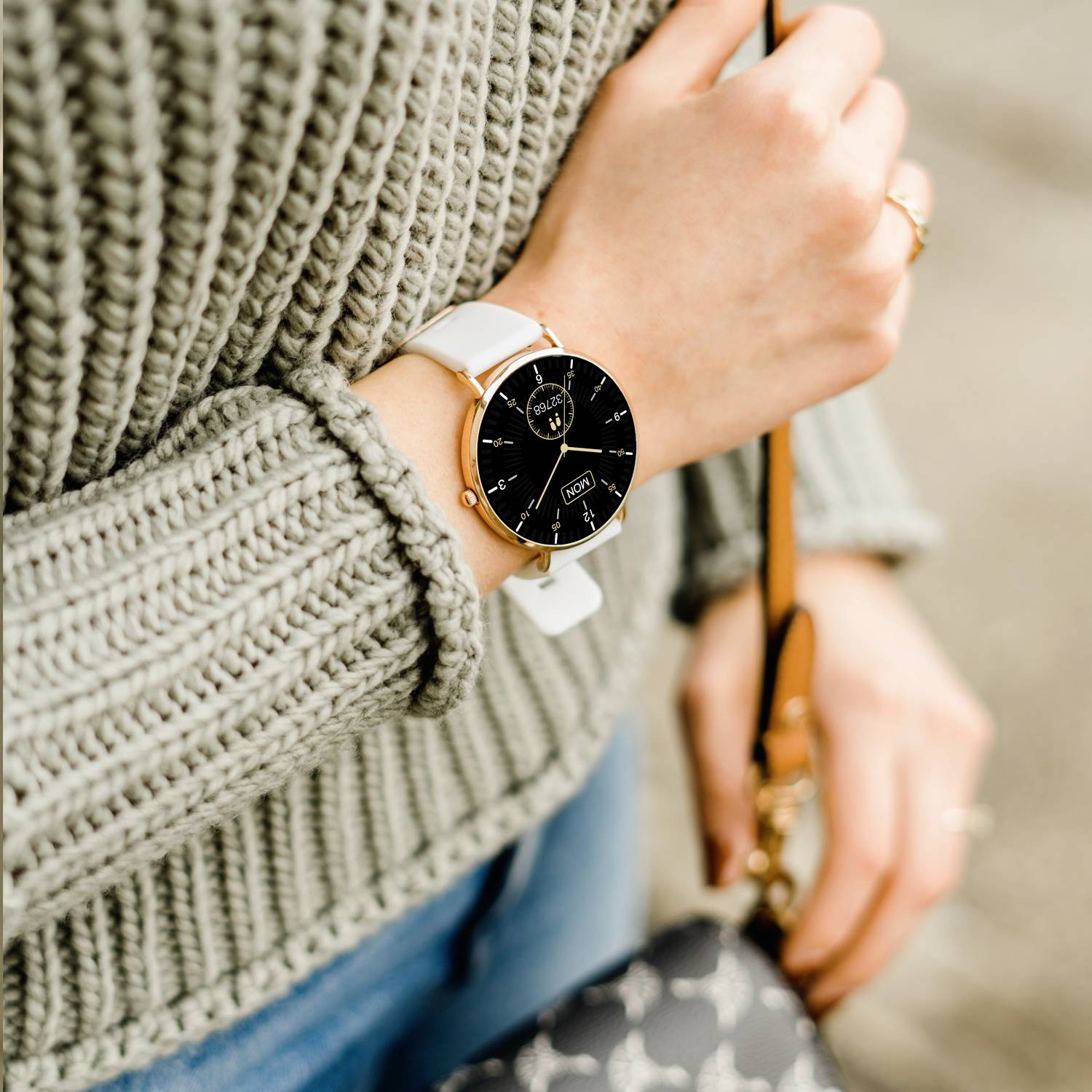 Osoba nosi elegancki zegarek na rękę z czarną tarczą i złotymi detalami. Trzyma brązową torbę.