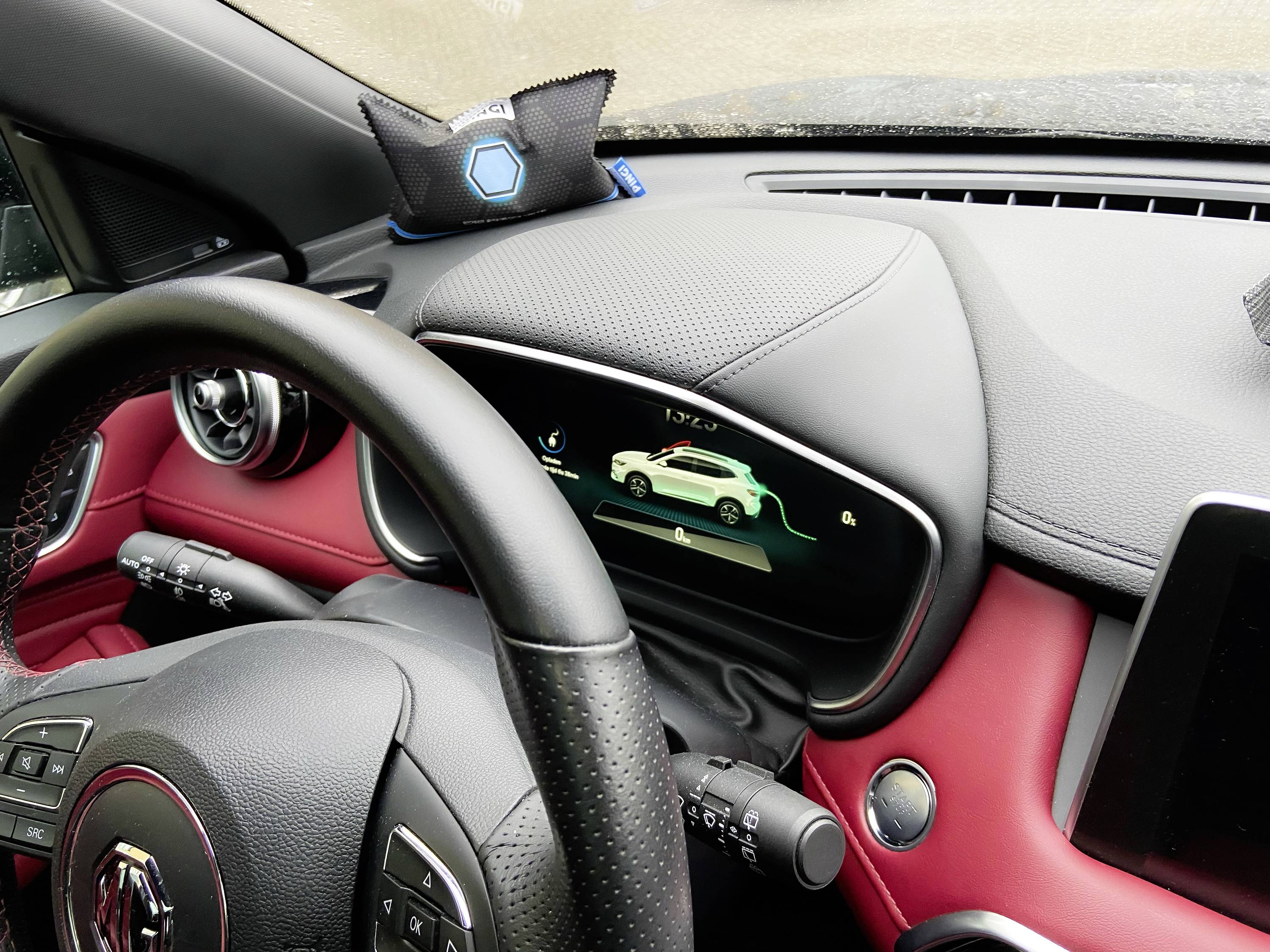 Kokpit samochodu z kierownicą, cyfrowym wyświetlaczem przedstawiającym samochód oraz czerwono-czarnymi akcentami we wnętrzu.