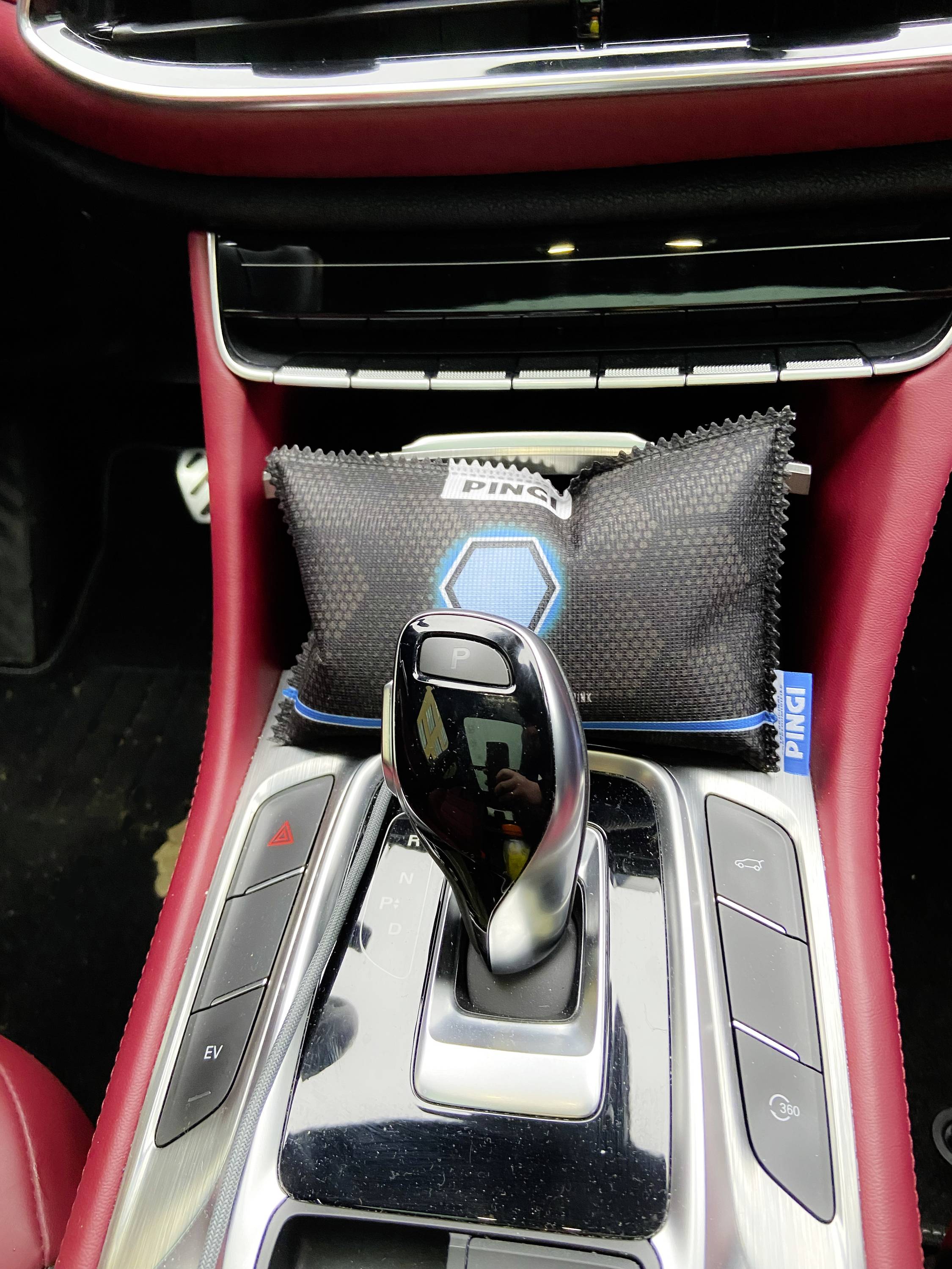 Wnętrze samochodu z czerwoną skórą, prezentujące konsolę środkową z dźwignią zmiany biegów oraz małym uchwytem na poduszkę za dźwignią.