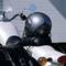 Srebrny kask motocyklowy jest przymocowany do siedzenia białego motocykla. Po lewej i prawej stronie widoczne są czarne sakwy.