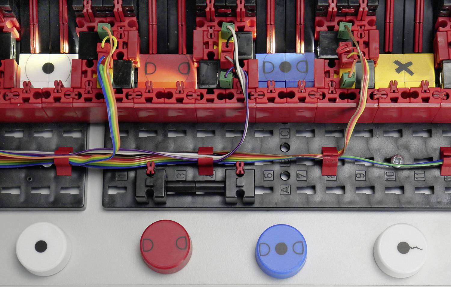 Wielokolorowe przewody i kolorowe przyciski w urządzeniu technicznym. Przyciski są czerwone, niebieskie i żółte z różnymi oznaczeniami.
