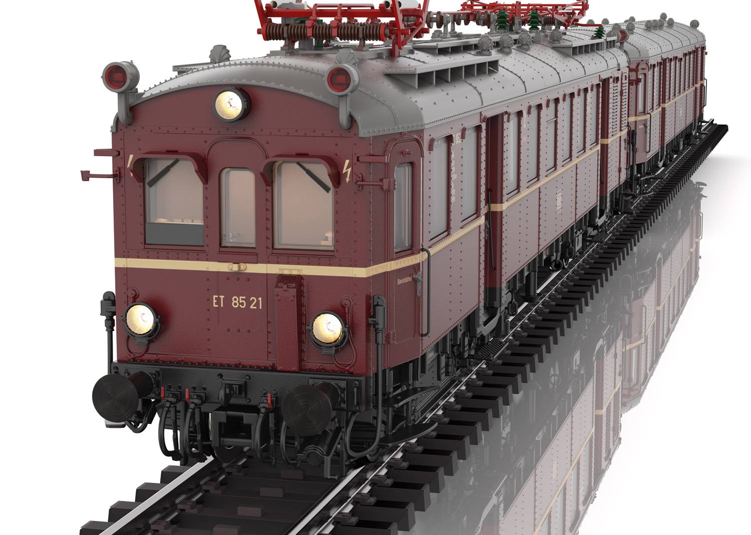 Historyczny czerwony wagon silnikowy z reflektorami na torach, widok z przodu. Wagon posiada okna, łukowy dach i przewody trakcyjne.