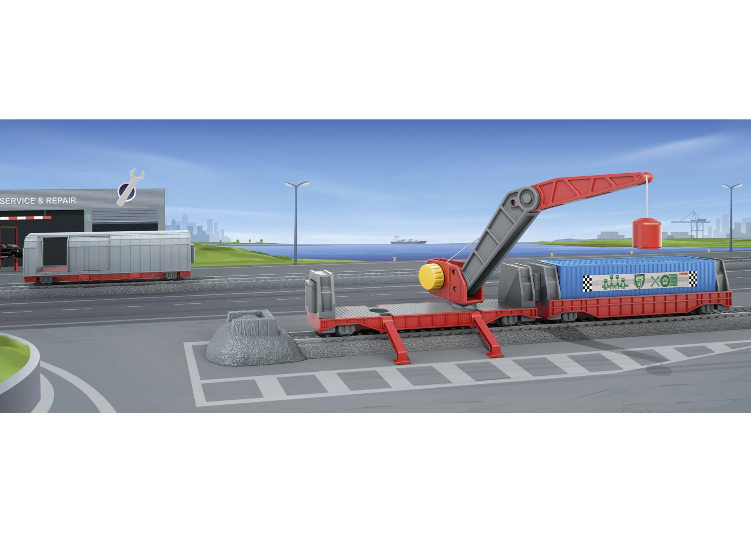 Zabawkowy krajobraz z czerwoną stacją załadunkową i niebieskim pociągiem kontenerowym. W tle budynek z napisem 'Serwis & Naprawa'.