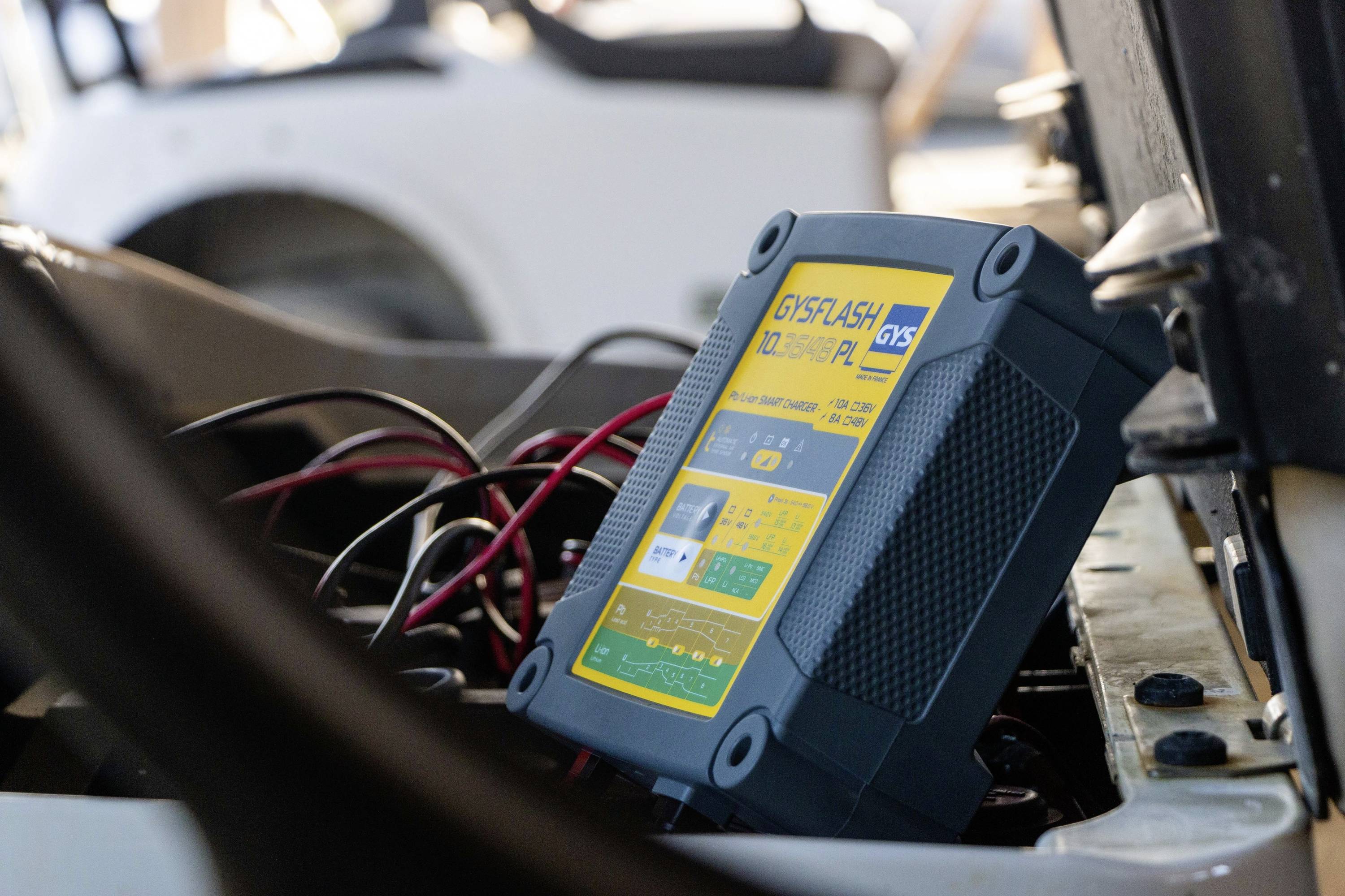 Ładowarka akumulatorowa jest podłączona do akumulatora pojazdu. Urządzenie wyświetla informacje o pracy na żółtym ekranie.