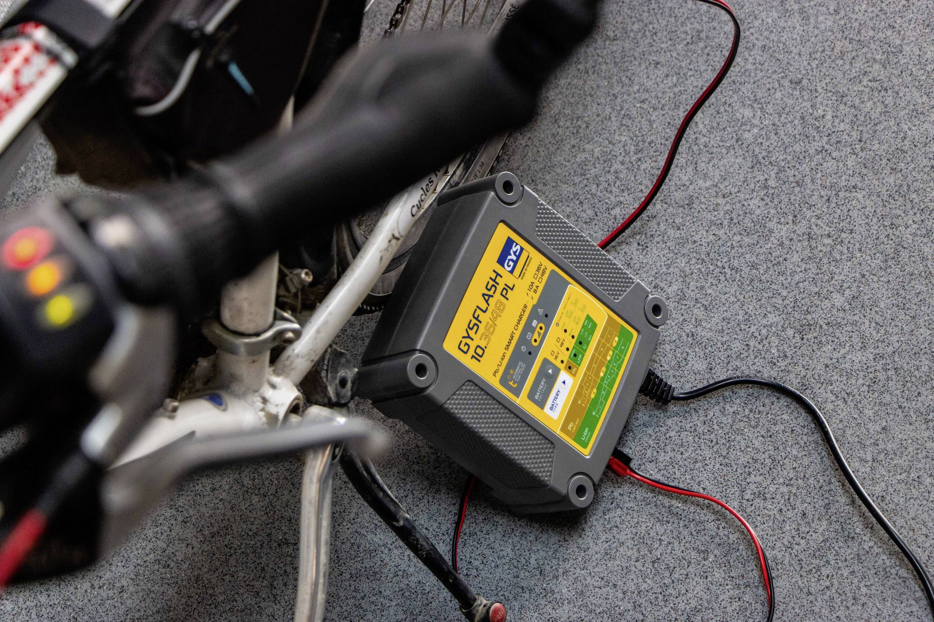 Ładowarka do baterii jest podłączona do roweru stojącego na dywanowej podłodze. Wyświetlacz pokazuje szczegóły procesu ładowania.
