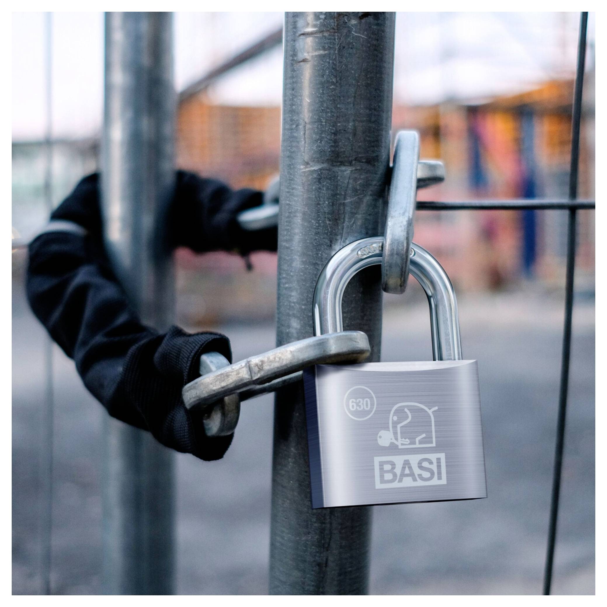 Rękawiczkowana dłoń używa nożyc do cięcia śrub na kłódce przymocowanej do metalowej bramy, sugerując włamanie lub naruszenie bezpieczeństwa.