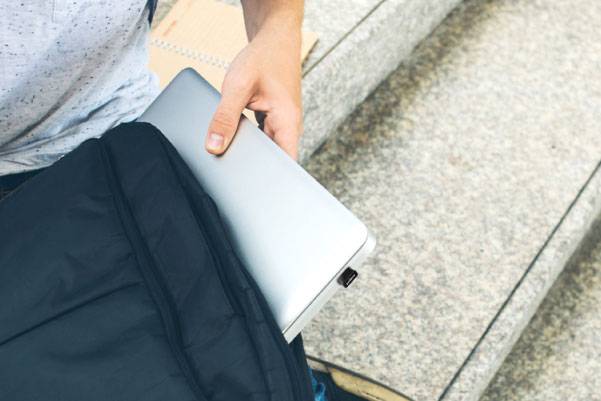 Osoba siedząca na schodach wkłada laptopa do plecaka.