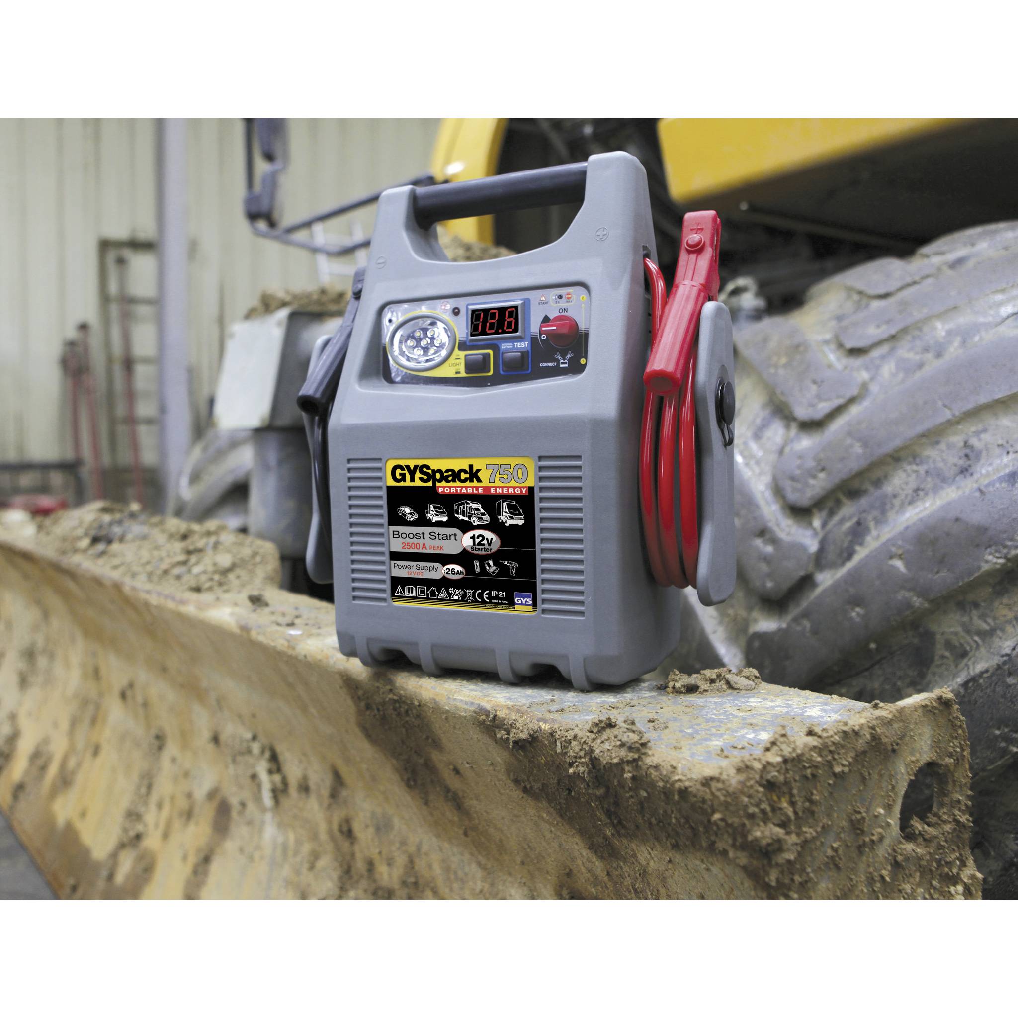 Przenośny rozrusznik awaryjny 'GYSpack 750' z wyświetlaczem i przewodami, umieszczony na brudnym ładowarce kołowej.
