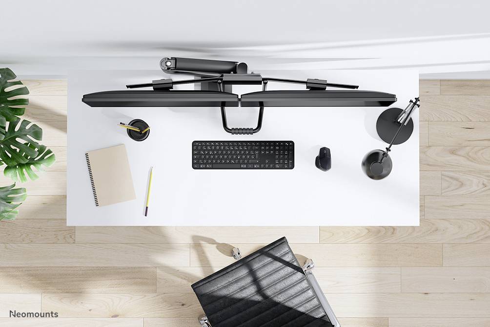 Nowoczesne stanowisko pracy z perspektywy z góry: biały stół z klawiaturą, myszą, notatnikiem, długopisem, ramieniem monitora i lampką biurkową.