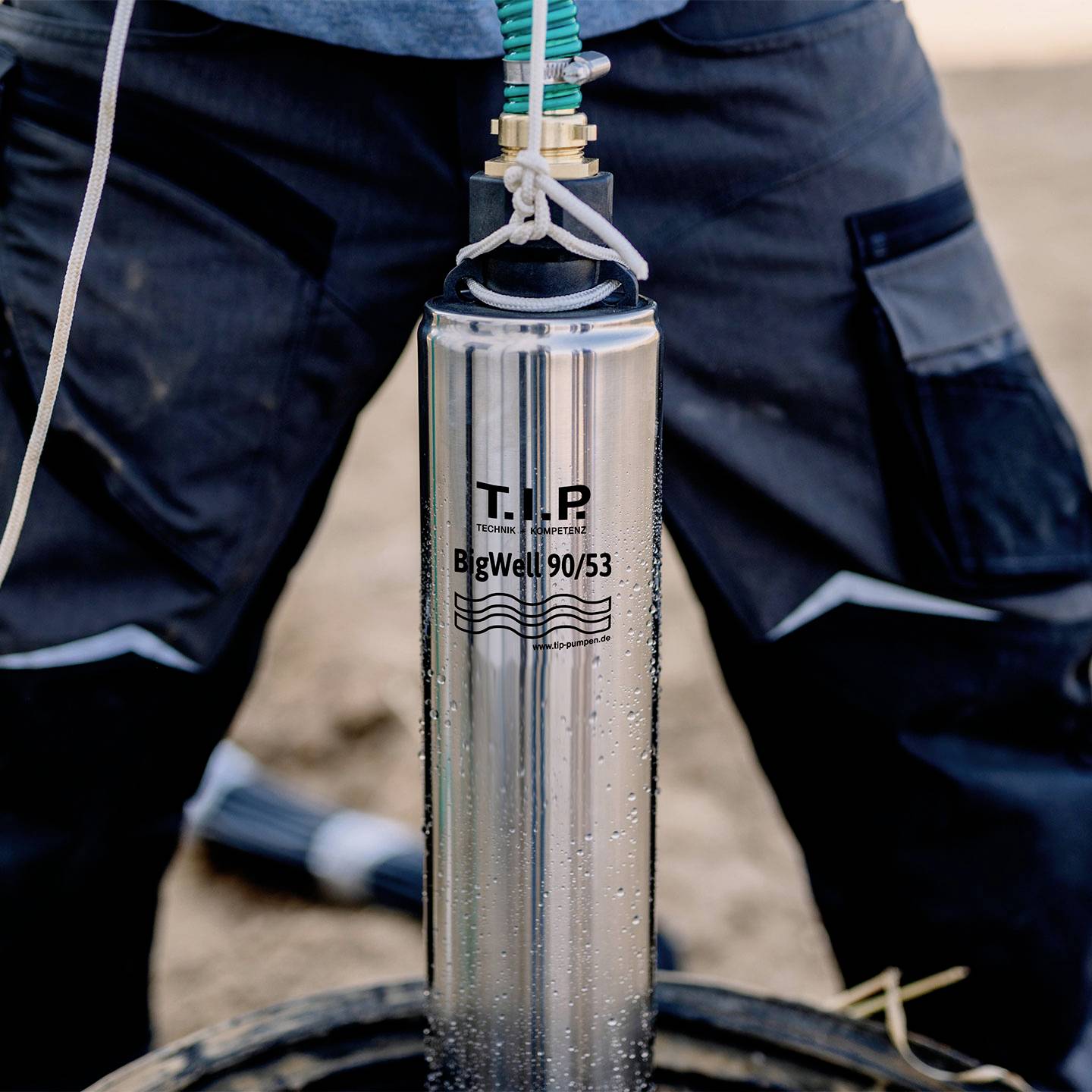 Osoba trzyma srebrny cylinder z napisem 'BigWell 90/53', będący częścią systemu wiertniczego do studni, na wolnym powietrzu.