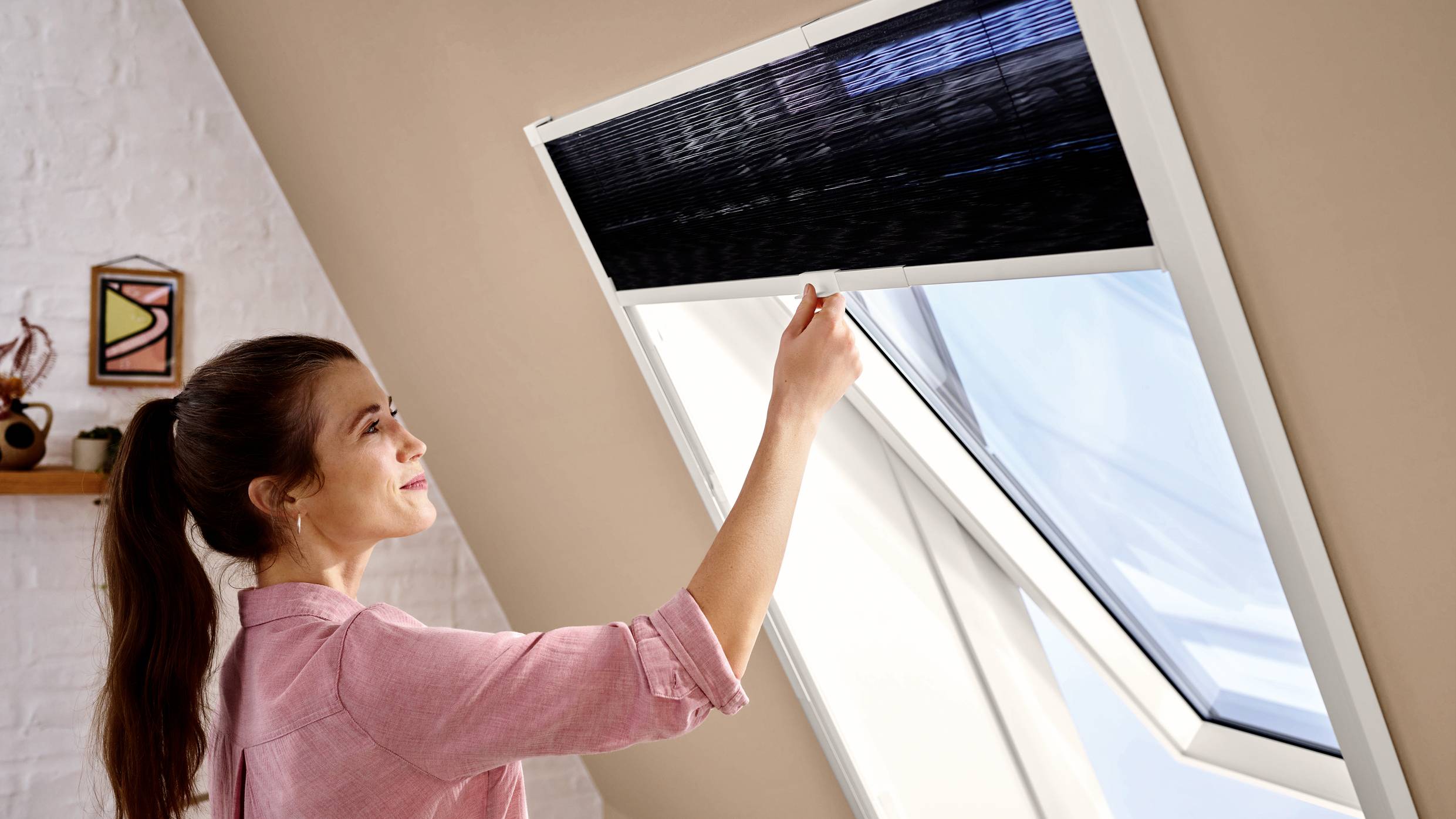 Kobieta otwiera skośne okno na strychu. Światło słoneczne wpadające przez okno rozświetla pomieszczenie.