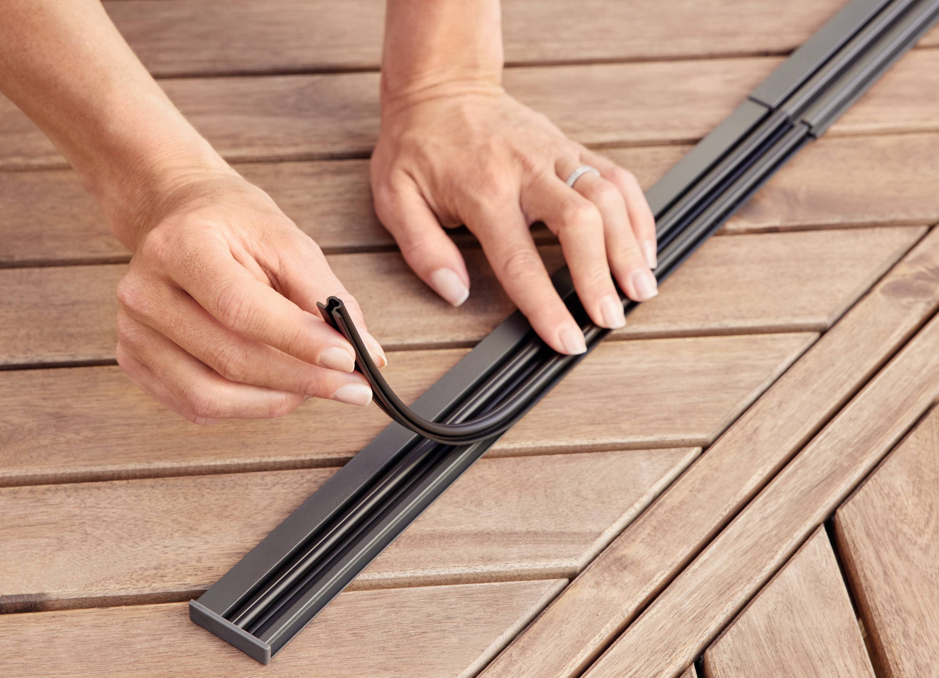 Ręce osoby instalują czarną uszczelkę w metalowej listwie na drewnianym stole.
