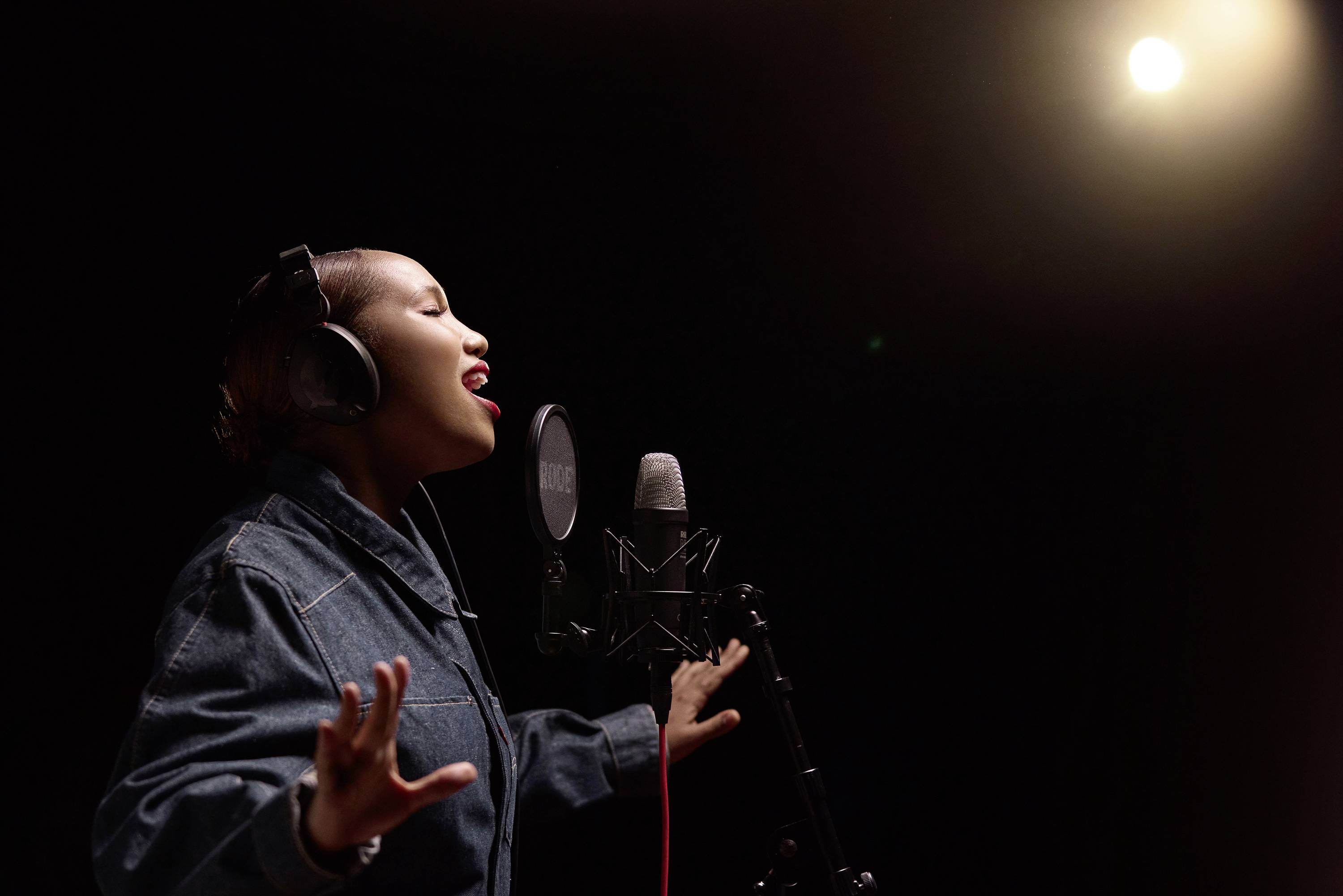 Osoba w słuchawkach śpiewa z pasją w mikrofon pod jasnym światłem reflektorów w studiu nagraniowym.