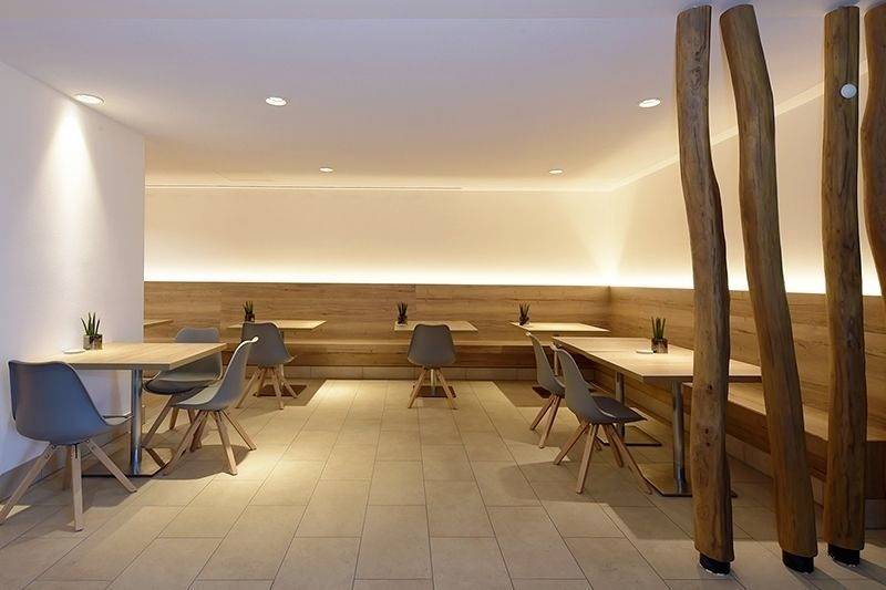 Nowoczesna, minimalistyczna jadalnia z drewnianymi stołami i ławami, ozdobiona pojedynczymi roślinami, oświetlona subtelnym, ciepłym światłem.