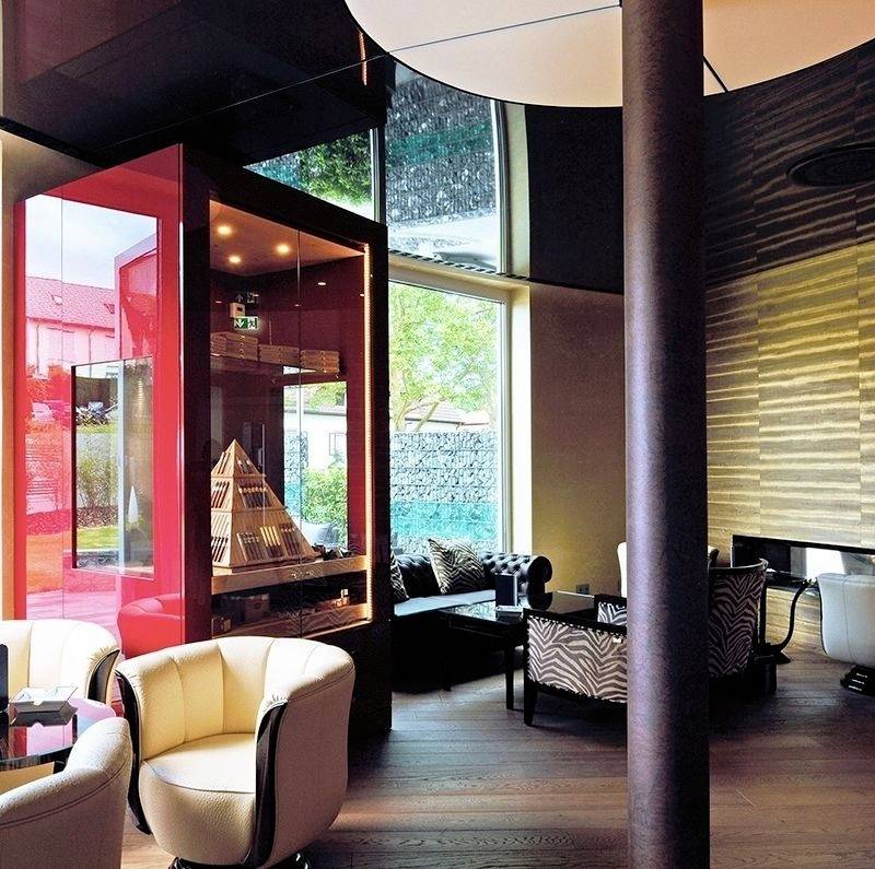 Nowoczesne lobby hotelowe z eleganckimi fotelami, dużymi oknami i czerwoną ramką wokół szafki wystawowej. Drewniana podłoga i ściany wyłożone drewnianymi panelami.