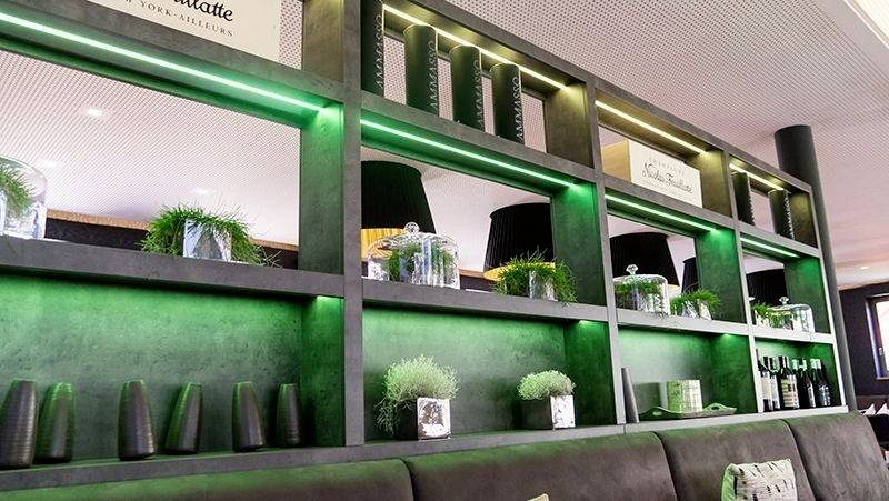 Stylowy regał z zielonym podświetleniem, roślinami dekoracyjnymi i butelkami. Nowoczesne, przytulne wnętrze kawiarni lub restauracji.