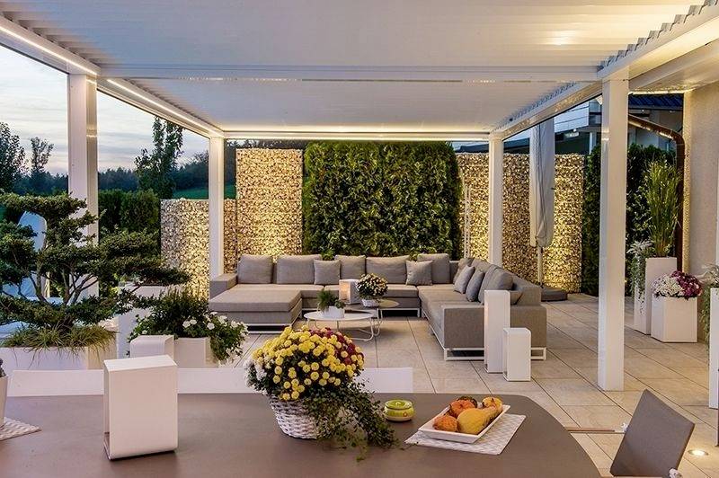 Nowoczesna przestrzeń tarasowa z dużymi sofami, dekoracyjnymi roślinami, meblami rattanowymi i nastrojowym oświetleniem o zachodzie słońca.