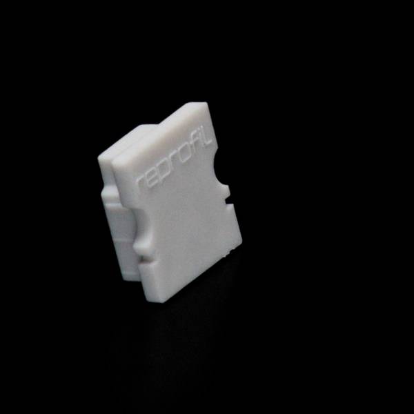 Biały, przypominający tworzywo sztuczne zacisk kablowy z napisem 'reprofil' na ciemnym tle.