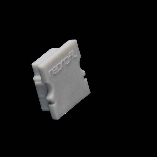 Biały, prostokątny obiekt z napisem 'reprofil' stoi pionowo na czarnym tle.