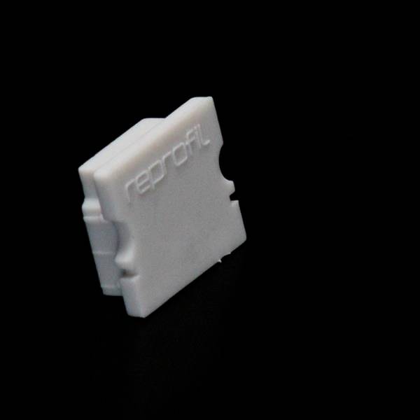 Biała, prostokątna plastikowa zatyczka z napisem 'reprofil' wykonanym szarą czcionką relief na czarnym tle.