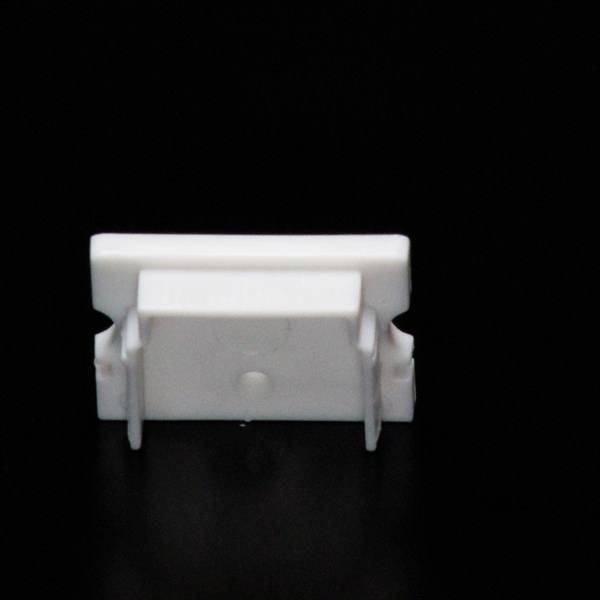 Mały biały obiekt plastikowy z klipsami, widziany z góry, na czarnym tle.