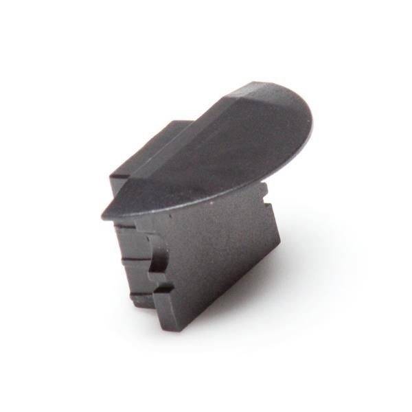 Czarny, klinowaty element z tworzywa sztucznego stojący na gładkiej powierzchni. Wygląda na mechaniczny składnik urządzenia.