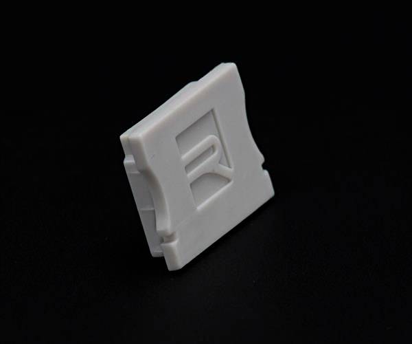 Mały, biały plastikowy klips z wytłoczonym literą 'R' na czarnym tle.