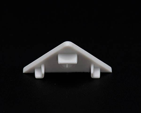 Biały, trójkątny obiekt z tworzywa sztucznego z czterema mocowaniami umieszczony na czarnej powierzchni.